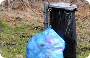 Kosz na śmieci. Obok stojący niebieski worek z odpadami.