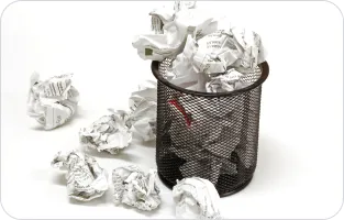 Kosz ze zgniecionymi kartkami papieru.